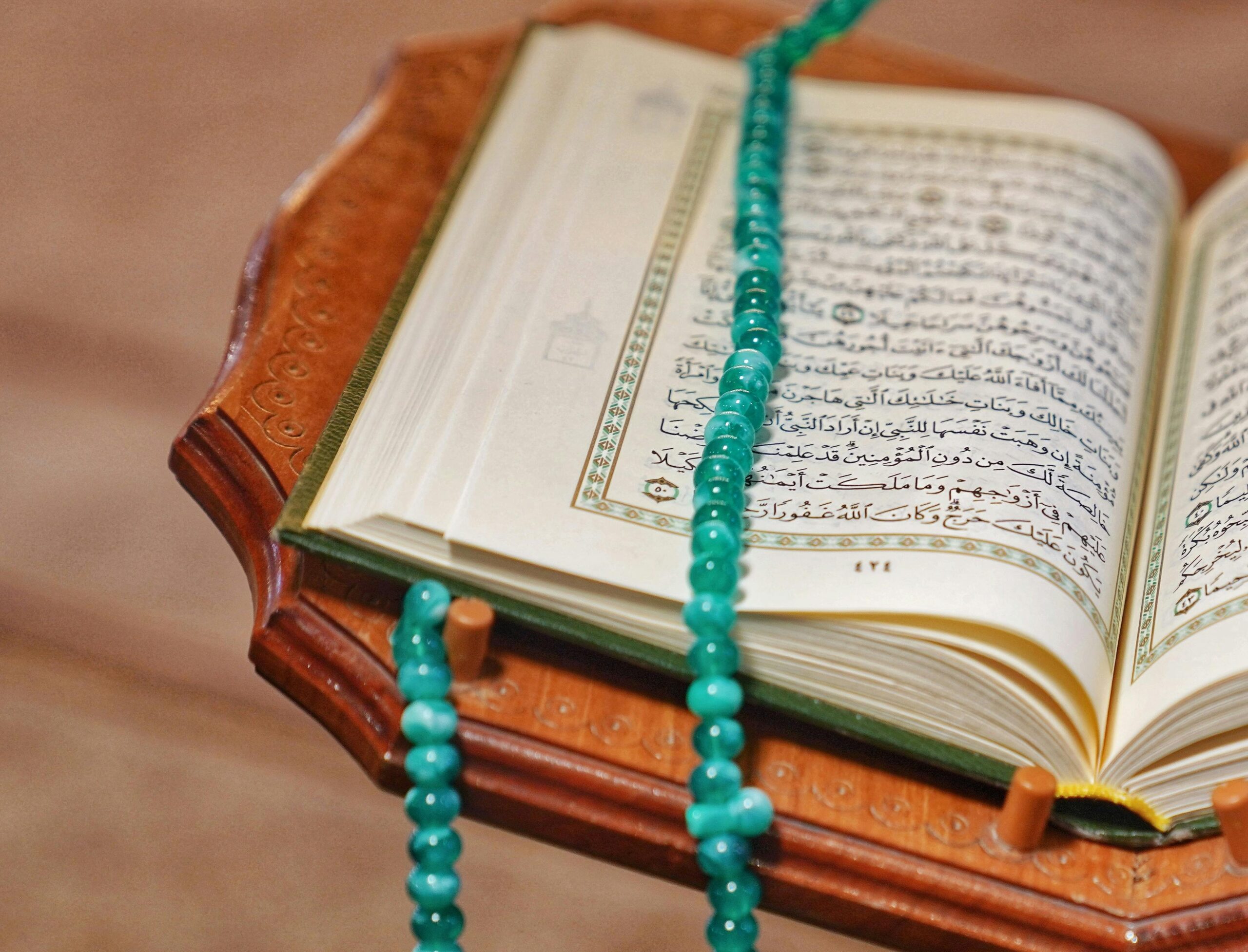 An open Quran with turquoise prayer beads rests elegantly on a carved wooden stand, symbolizing Islamic spirituality.